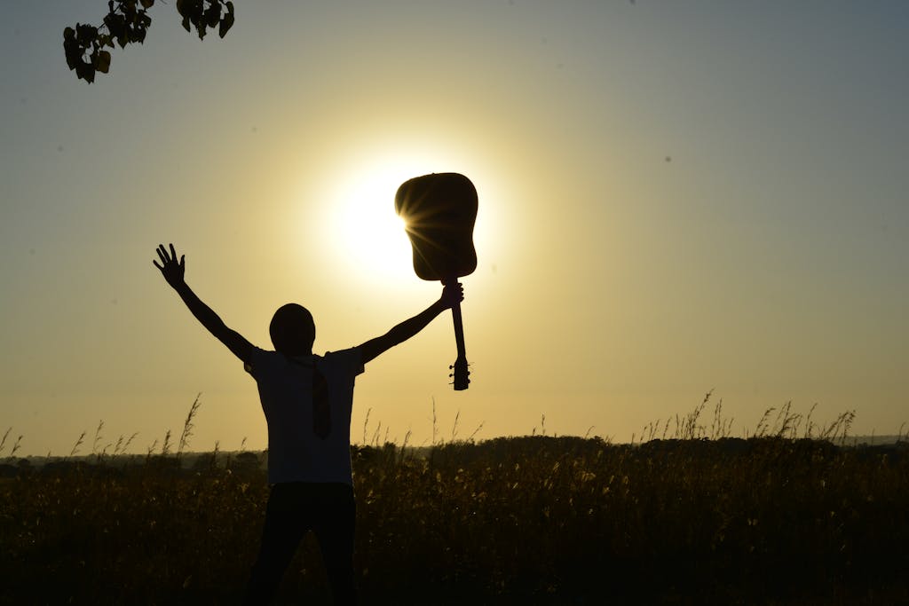 A young guitarist celebrates the sunrise with an acoustic guitar, creating a dramatic silhouette.