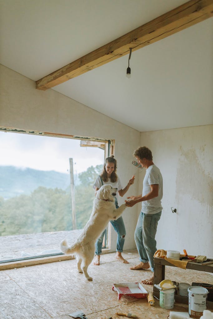 A couple enjoys a playful moment with their dog while renovating their home with large open views.