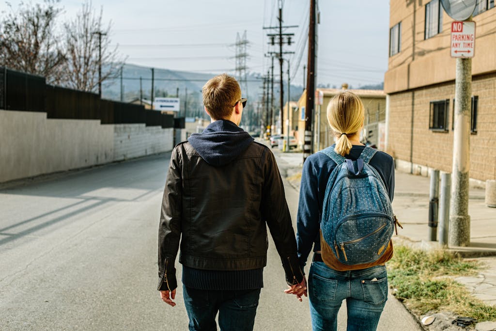 A couple walks hand in hand on an urban street, back view, showcasing companionship and daily life.