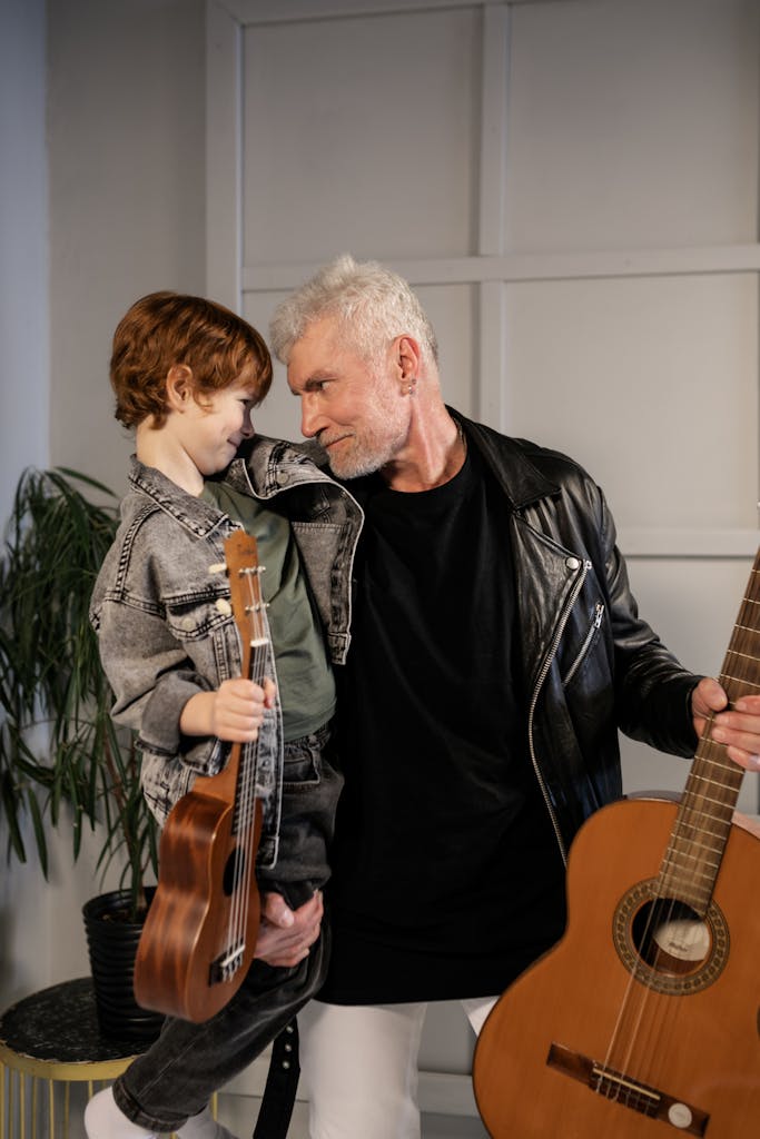 A grandfather and grandson bond over music, each with a guitar, indoors.