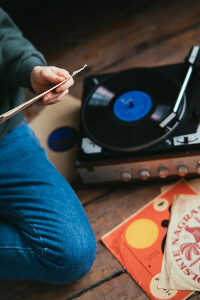 A person sits cross-legged enjoying vintage vinyl records on a turntable.
