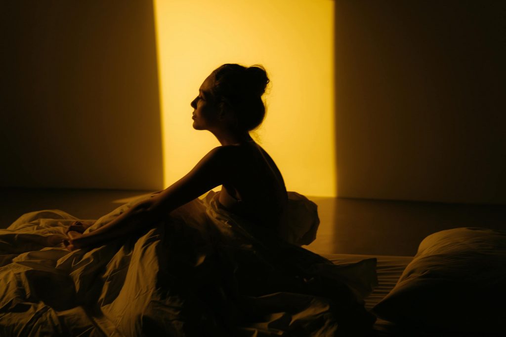 A silhouette of a woman sitting in bed with warm sunlight streaming in.