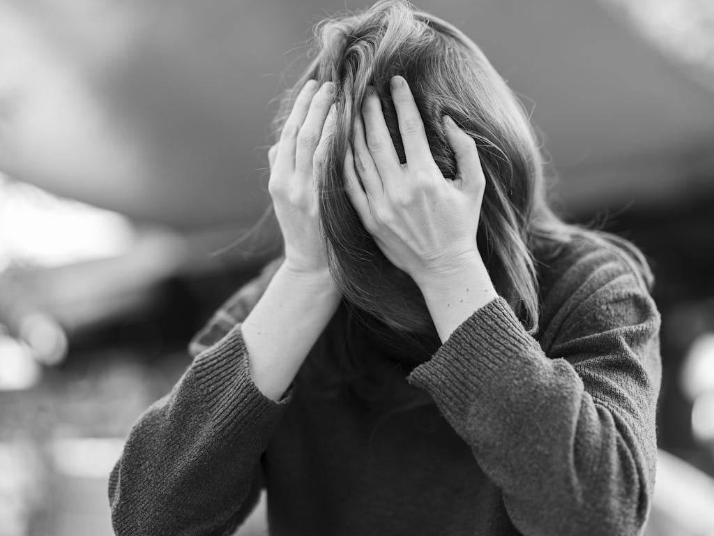 A woman in distress holding her head in her hands, captured in a dramatic black and white portrait.