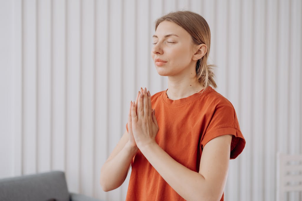 A woman in orange practices meditation indoors, expressing mindfulness and concentration.
