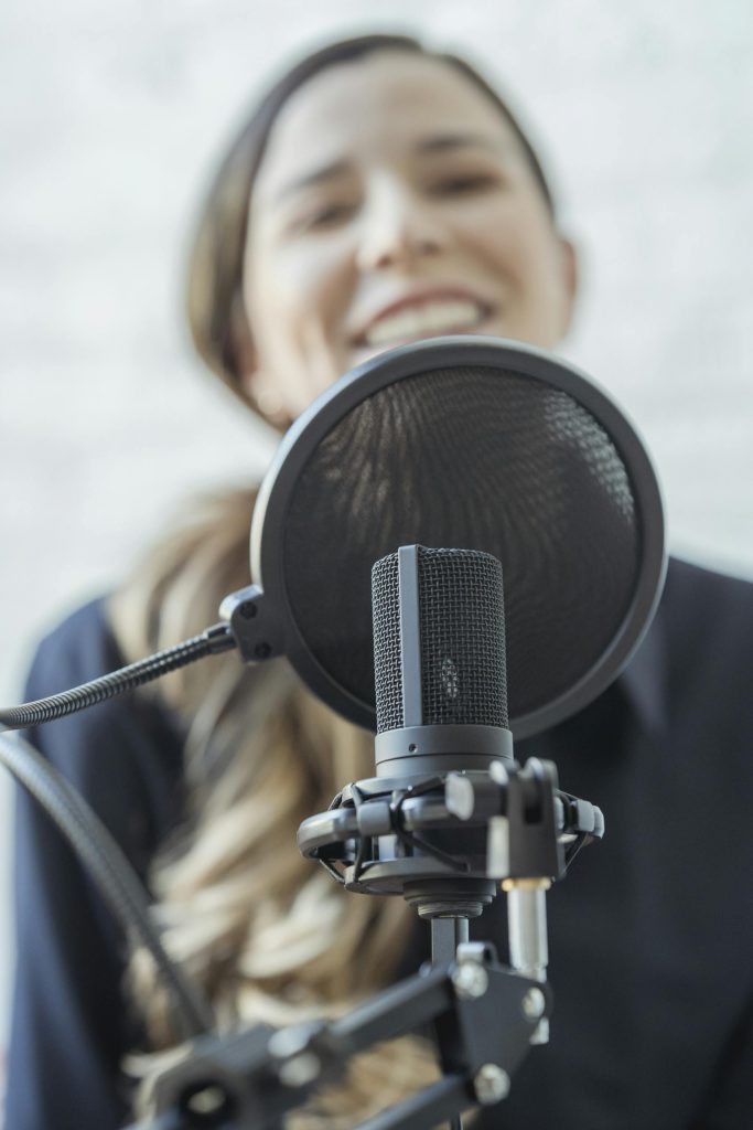 A woman smiles while recording with a professional microphone. Recover from depression with Musician Therapy Collective