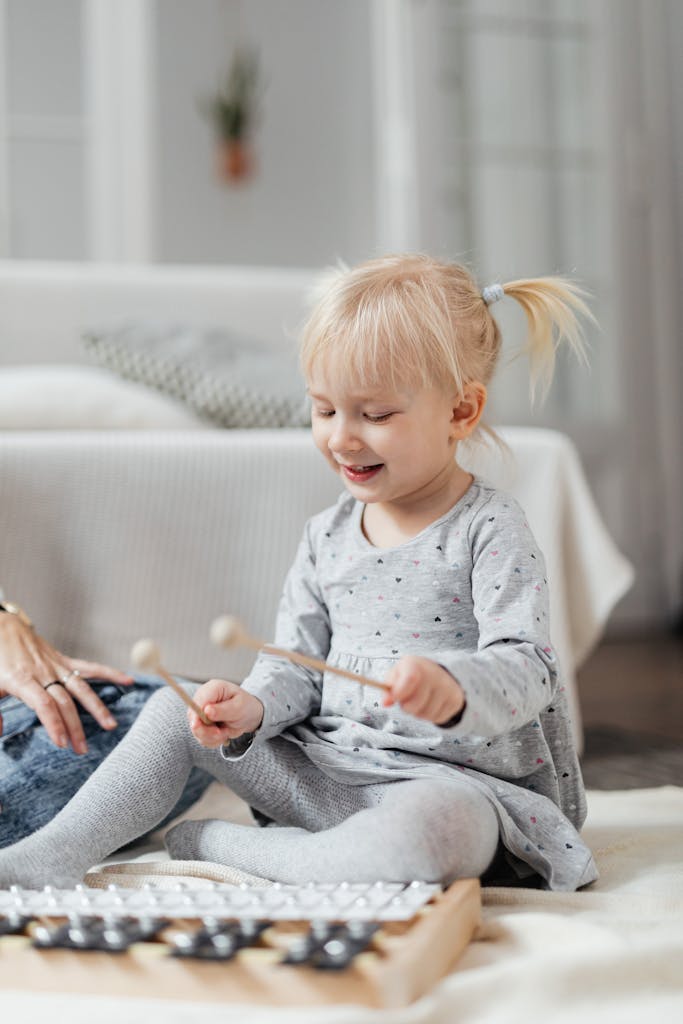 A young girl joyfully plays a xylophone indoors, expressing creativity and enjoyment.