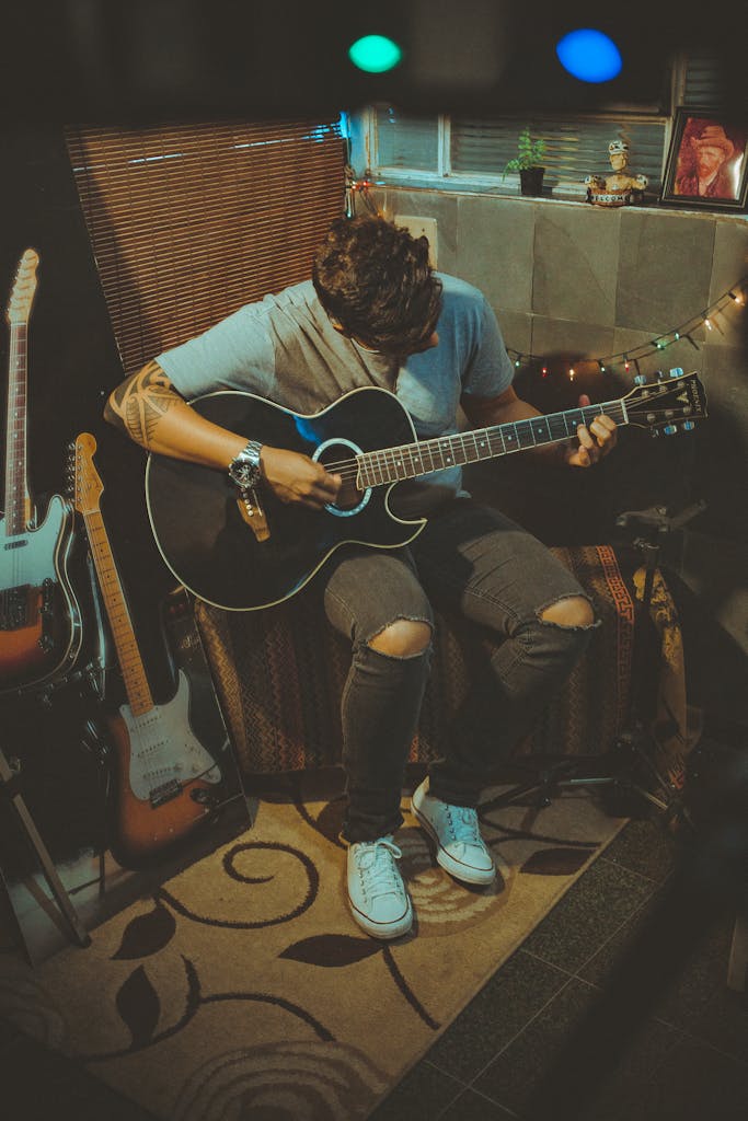 A young man plays guitar in a cozy, dimly lit room, creating a musical atmosphere.