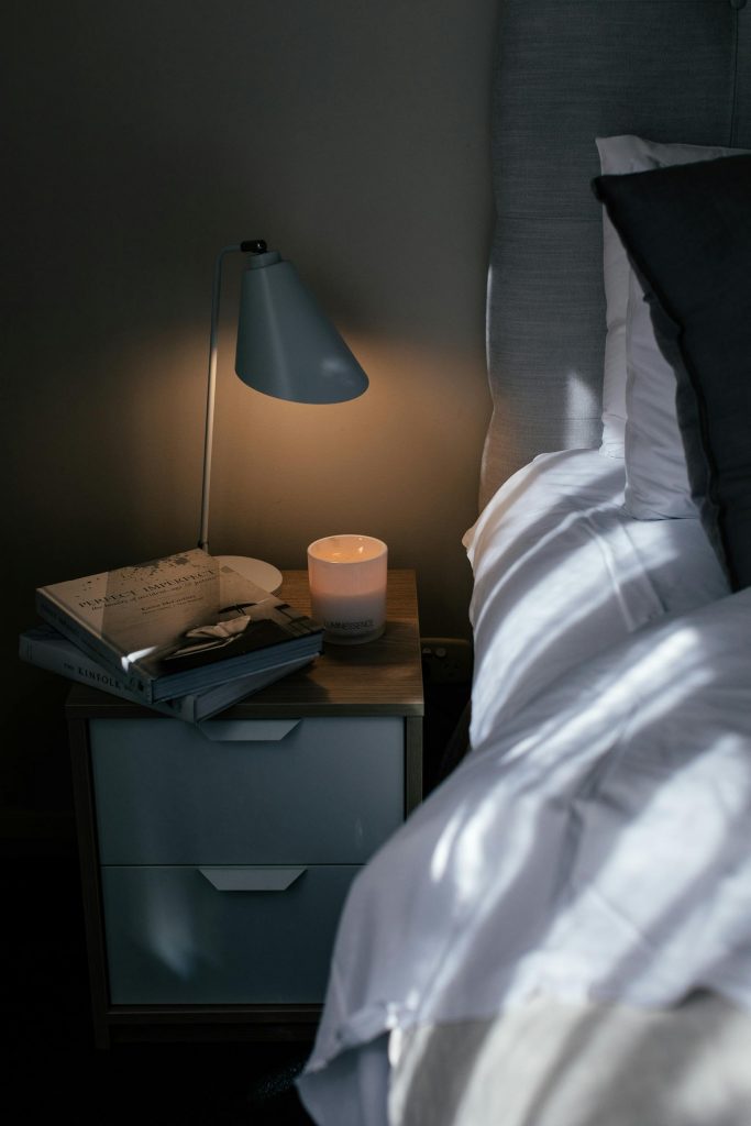 Cozy bed with crumpled sheet and pillows near nightstand with textbooks and lamp in bedroom