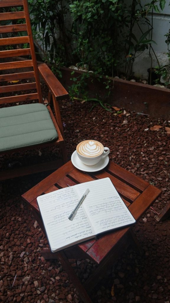 Cozy outdoor setting with cappuccino, notebook, and pen on a wooden table. Perfect for relaxation.