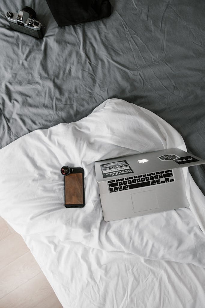 Minimalist flatlay of a remote work setup with laptop and smartphone on a bed.