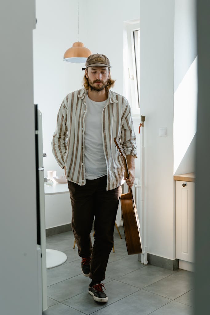 Stylish young man with a guitar casually walks in a well-lit room.