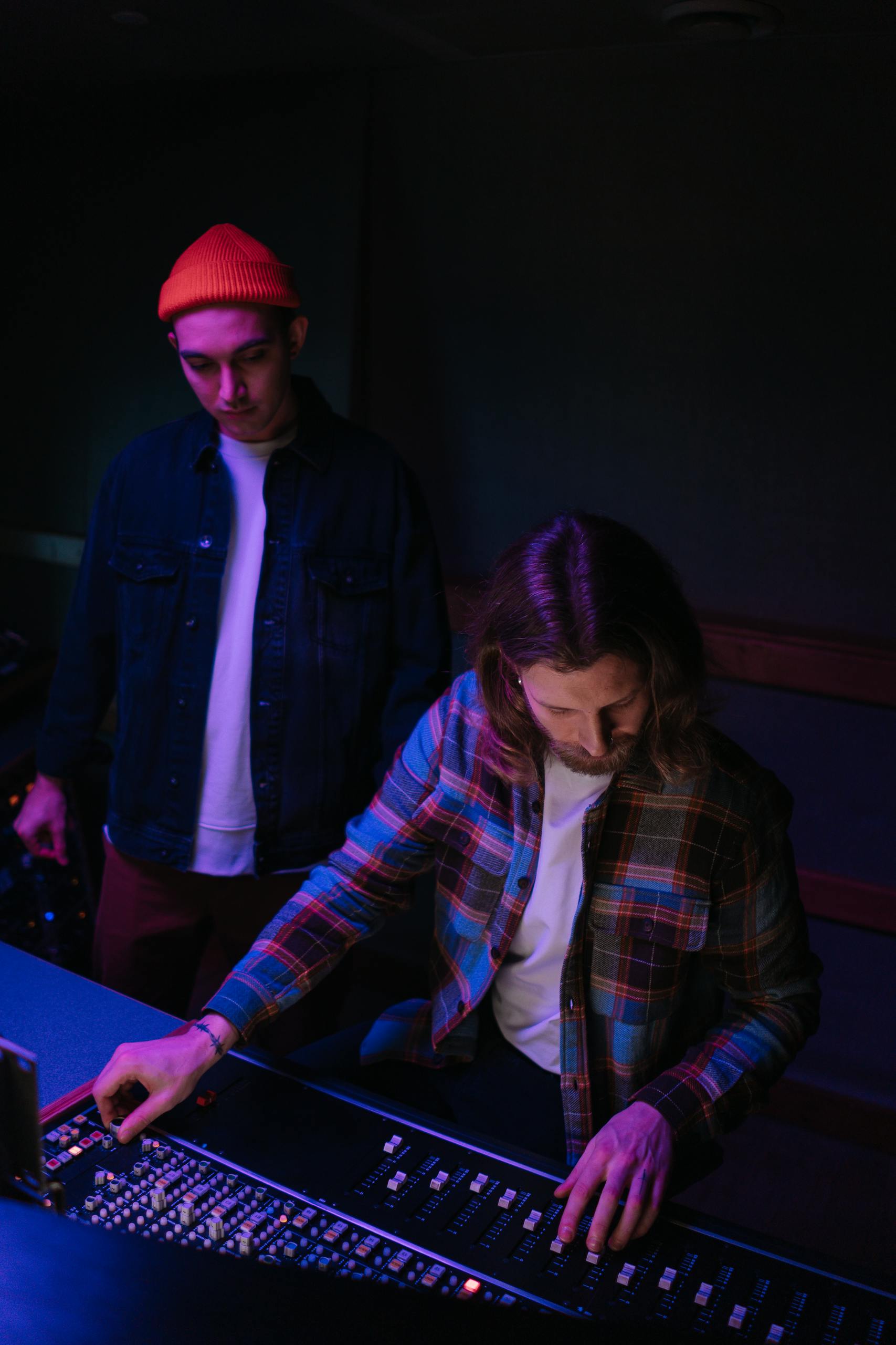 Two audio engineers collaborate at a mixing console in a dimly lit studio.