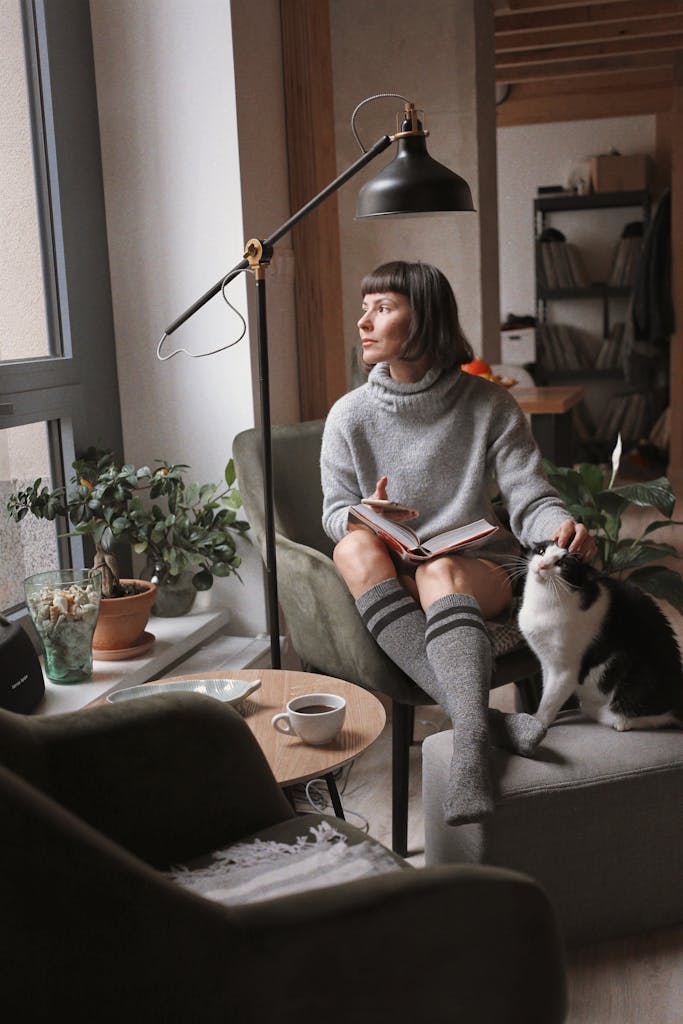 Woman enjoys a relaxing moment with a book and cat in a cozy living room setting.
