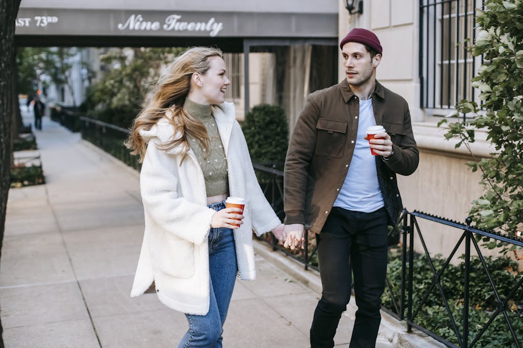 Young couple holding hands and enjoying a coffee while strolling on a city street.