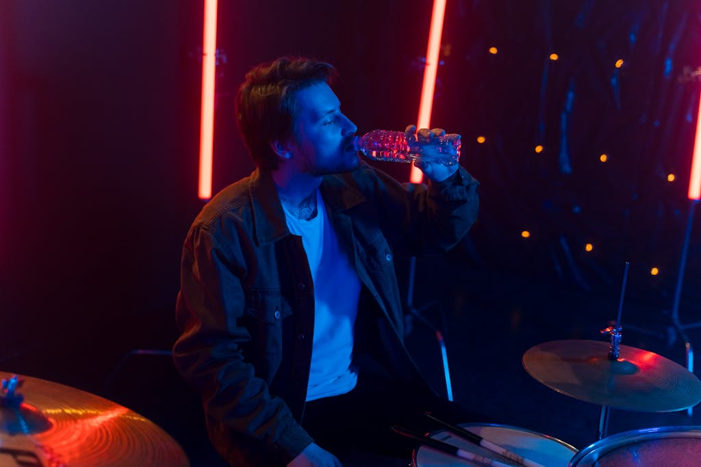 Young drummer in a studio setting staying hydrated with a water bottle.