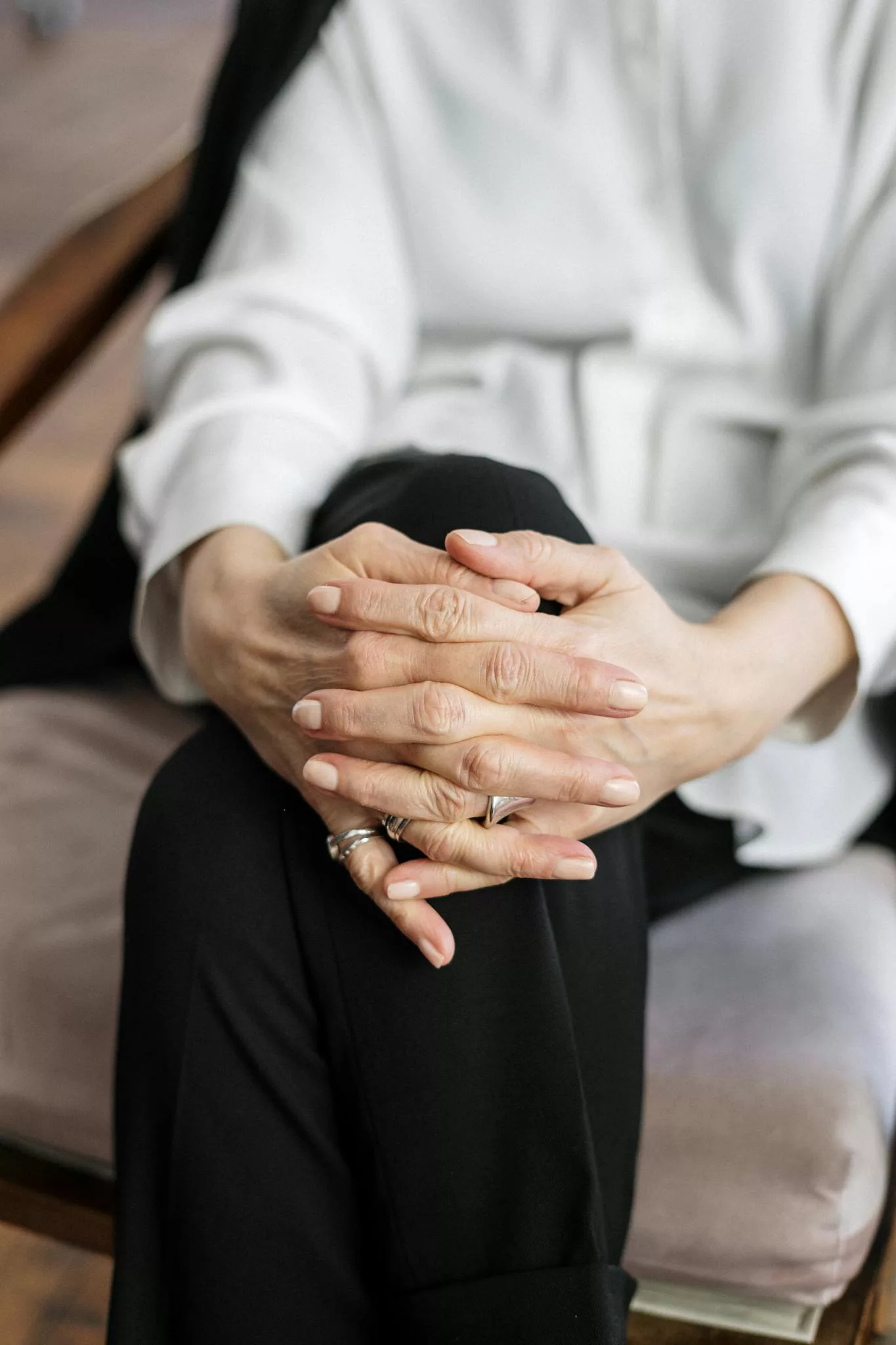 Close-up of a woman's hands clasped, seated in an office setting, exuding professionalism.