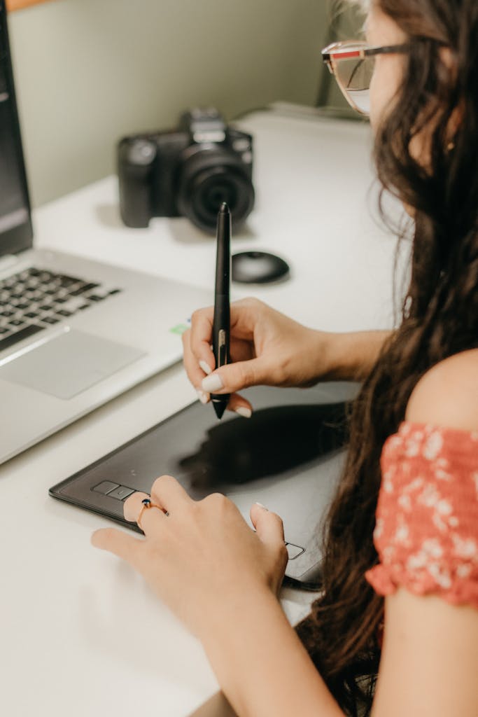 Female graphic designer working with a tablet and laptop in a modern workspace.