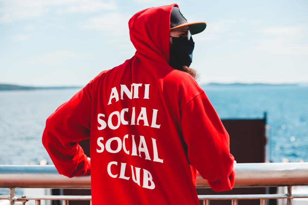 Individual wearing red hoodie with text at seaside. Urban street style.