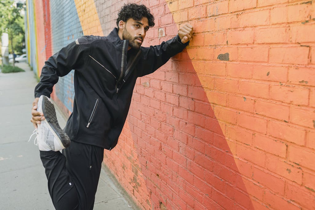 Athletic man in sports attire stretching against a vibrant mural wall outdoors.